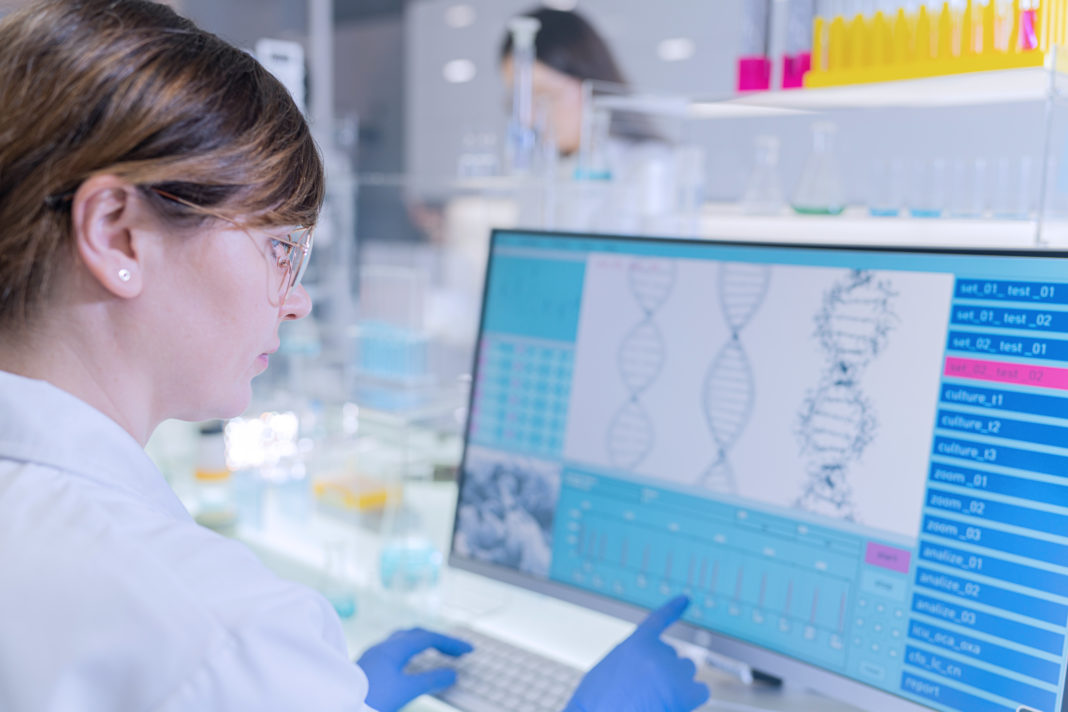Female research team studying DNA samples. Computer screens with DNA helix in foreground